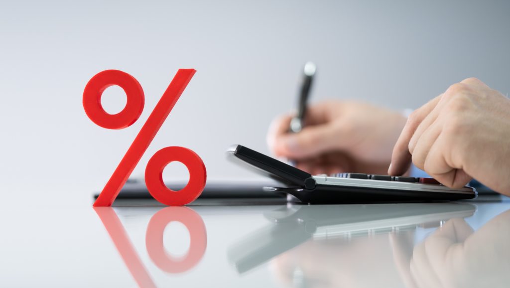 Close-up Of Red Percentage Symbol In Front Of Businessperson Calculating Invoice
